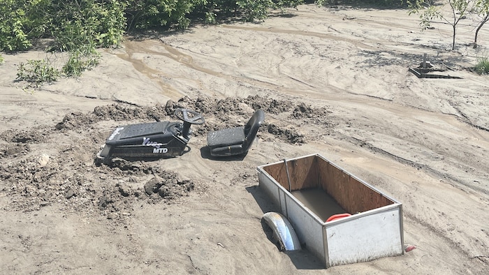 Une cour envahie de boue, dans laquelle on voit un tracteur à gazon et une remorque ensevelis.