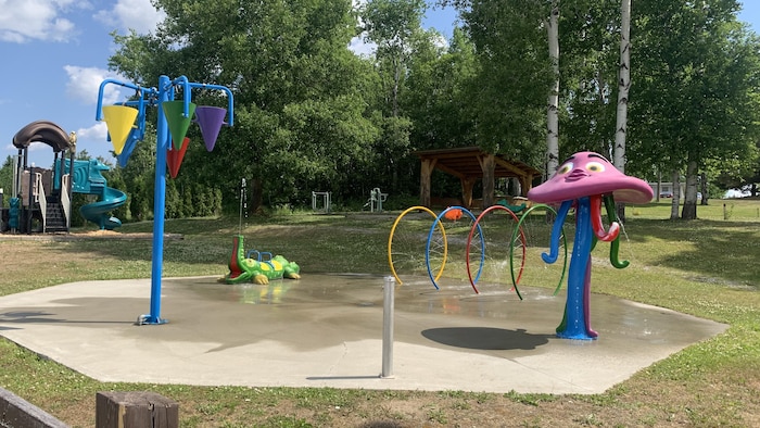 Des jeux d'eau dans un parc de Rivière-Héva, avec une glissoire et un boisé en arrière-plan.