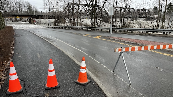 Des cônes empêchent la circulation. On voit au loin que la rivière déborde sur la chaussée.