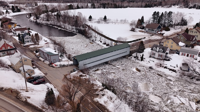 Vue aérienne d'un village bordant une rivière à moitié couverte de glace flottante.