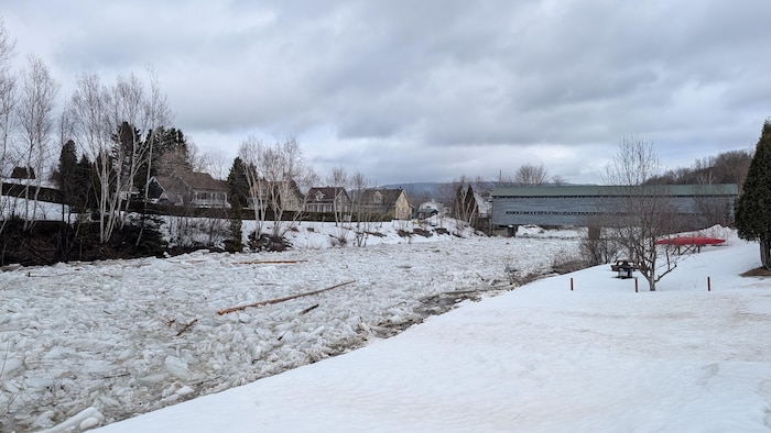 Une rivière couverte de glace flottante. Un pont couvert des maisons sont visibles.