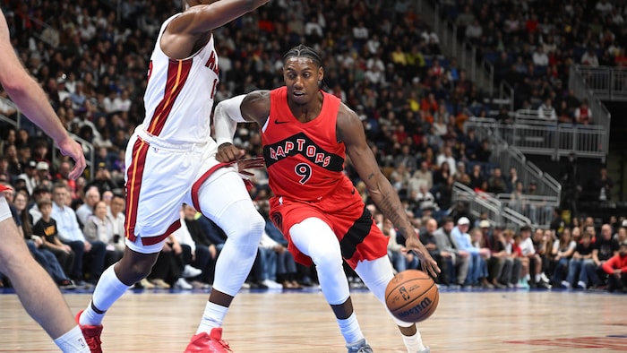 RJ Barrett dribble avec le ballon en repoussant du bras un joueur du Heat de Miami.