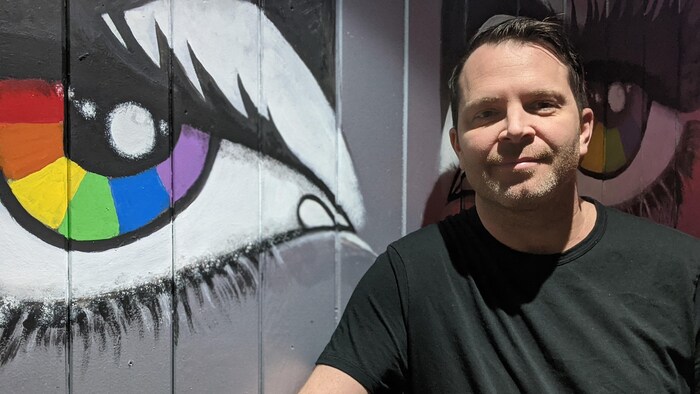 Rob Browastzke devant une peinture aux couleurs du drapeau de la fierté.