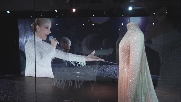 Une robe est présentée devant un écran diffusant des images de Céline Dion.
