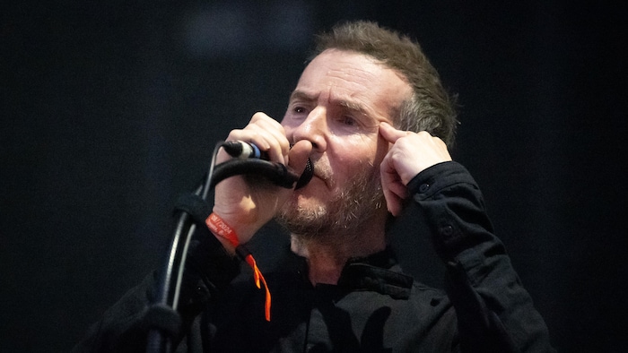 Le chanteur en prestation sur scène, un doigt pointé sur la tempe. 