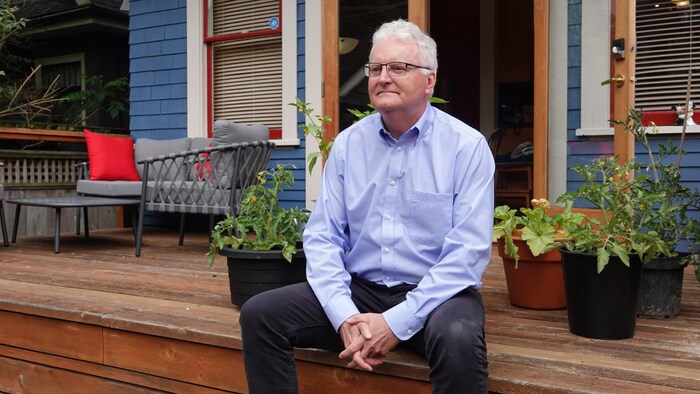 Robert Grant est assis sur son patio derrière sa maison, devant des plants de légumes.