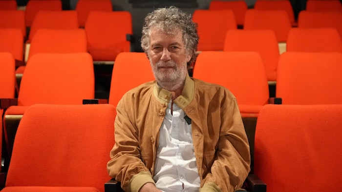 Portrait de Robert Morin assis dans un banc de cinéma.