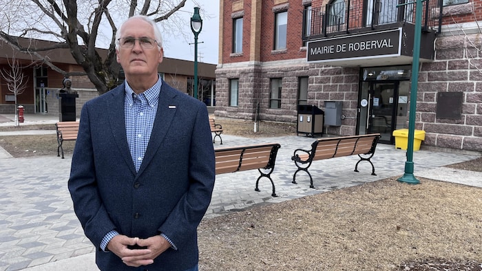 Un homme en complet pose, les mains jointes, devant la mairie de Roberval.