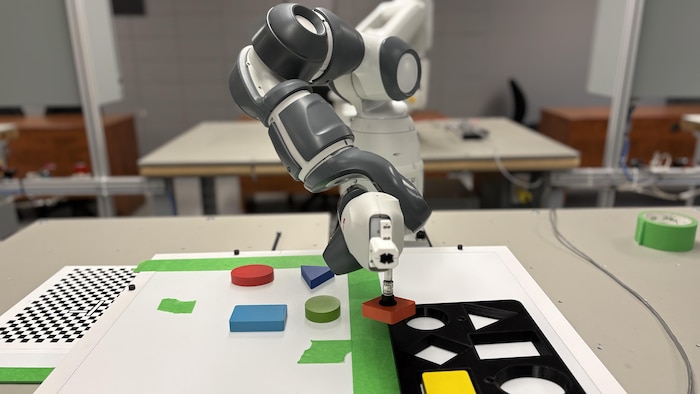 Dans un laboratoire de robotique d'un cégep, un robot déplace des pièces de casse-tête de bois de couleurs et de formes différentes.