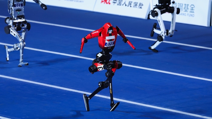 Trois robots humanoïdes courent sur une piste d'athlétisme.