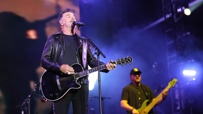 Le chanteur est accompagné d'un bassiste pendant un spectacle. Il s'accompagne lui-même à la guitare.
