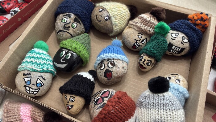 Des pierres peintes avec des motifs de visages, recouvertes de petits bonnets.