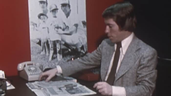 Rodger Brulotte, jeune, assis à un bureau en train de consulter des documents.