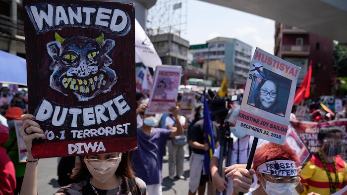 Mga tao na may hawak ng placard na nagsasabing wanted Duterte, number one terrorist at hustisya.