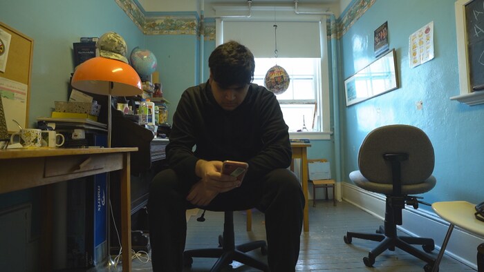 Manolo est assis et regarde son téléphone cellulaire.