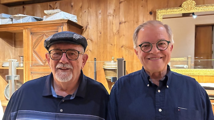 Roger Boudreau et Marcel LeFort posent côte à côte dans une pièce décorée comme au 18e siècle.