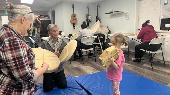 Un aîné, une femme et une fillette tiennent chacun un tambour.
