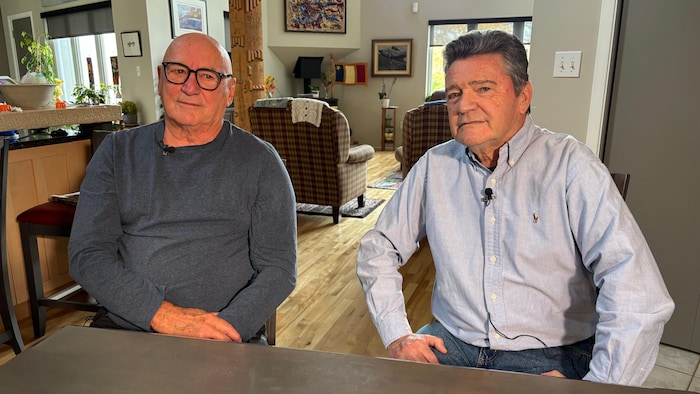 Roger LeBlanc et Bernard Richard posent pour la photo, assis à une table de cuisine dans une maison.