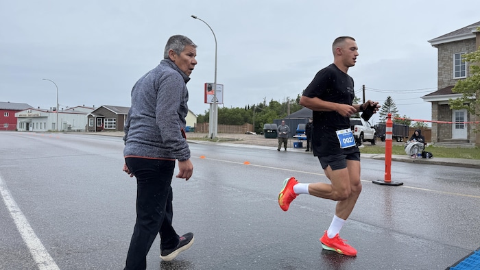 Roger Vachon s'apprête à traverser la rue, sous la pluie, alors qu'un marathonien le devance.