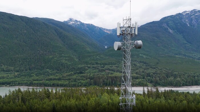 Une tour de communication devant une rivière et des montagnes.