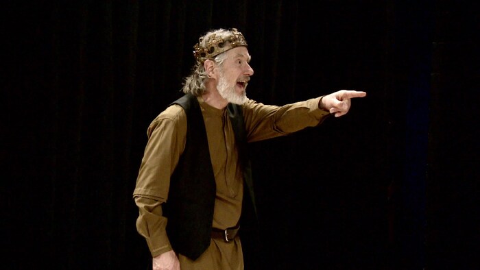 Bruce McKay dans le rôle du roi Lear, vêtu d'une couronne, pointe du doigt, son visage exprimant la surprise.