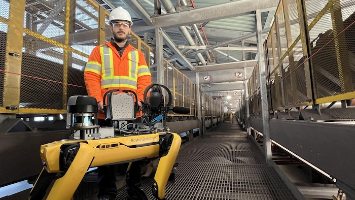 Romain Beaudoin en tenue de sécurité debout derrière un petit robot quadrupède.