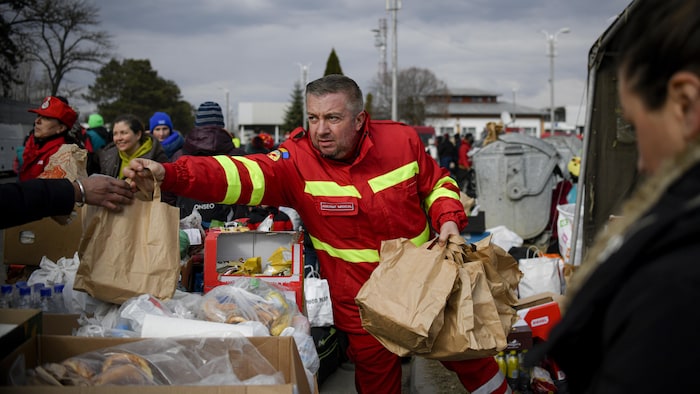 A man in uniform is handing out bags of groceries.