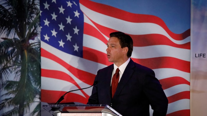 Ron DeSantis s'exprime devant un drapeau américain et un cocotier.