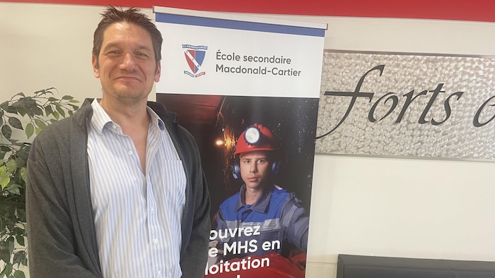 Ronald Filion devant une bannière du programme de majeur haute spécialisation de l'École secondaire Macdonald-Cartier.