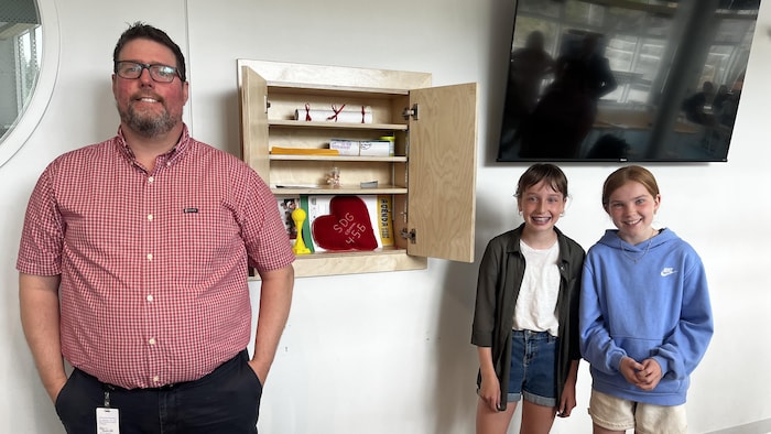 Un homme et deux filles posent devant une armoire