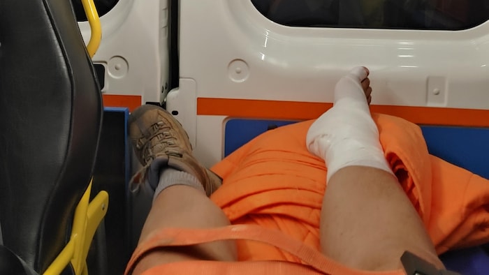 Deux jambes, dont une avec un pied dans un bandage, allongées sur une civière à l'intérieur d'un véhicule d'urgence.