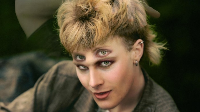 e visage d'un homme au regard double, coiffé un peu punk, avec une main fantomatique se glissant dans ses cheveux.
