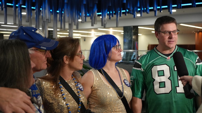Une famille parle au micro d'un journaliste. Tous sont vêtus des couleurs des Blue Bombers sauf Greg Stone qui est habillé d'un uniforme des Roughriders.