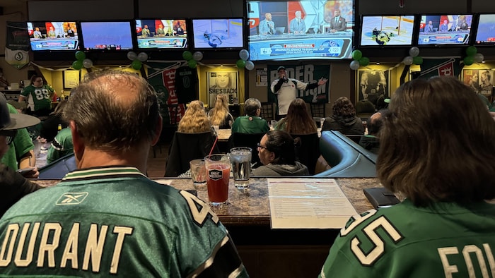 Des partisans portant des maillots des Roughriders présents dans un bar sportif devant des télévisions diffusant la rencontre.