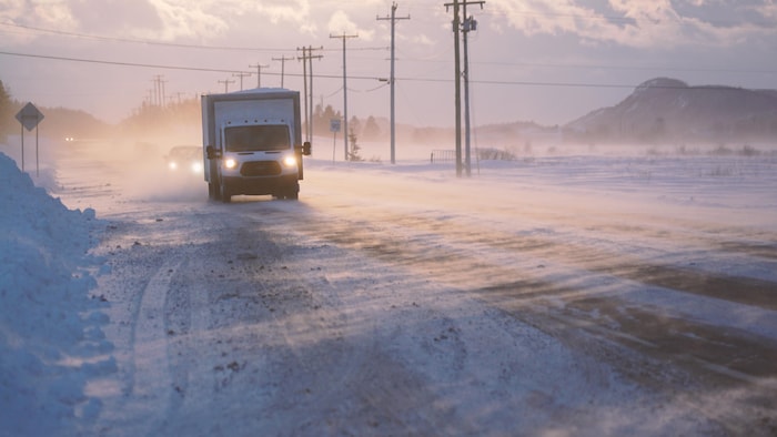 Un camion traverse la poudrerie sur une route de campagne.