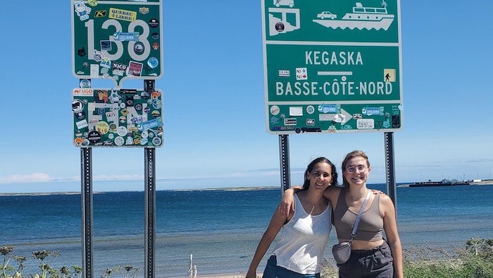 Deux personnes bras dessus bras dessous posent devant le panneau qui indique la fin de la route 138.