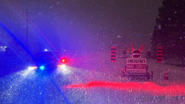Des pancartes indiquent que la route est fermée alors que la neige tombe abondamment sous le vent.