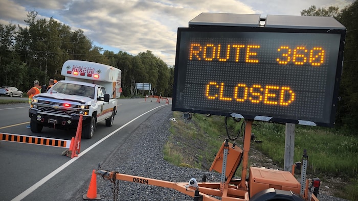 Un panneau qui indique que la route est fermée et un véhicule d'urgence stationné sur la route fermée. 