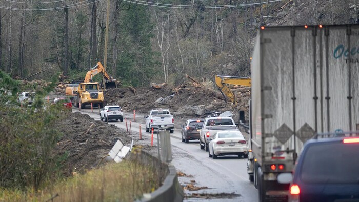 Des voitures circulent sur une seule voie de la route 7 pendant que des engins de chantier retirent des débris.