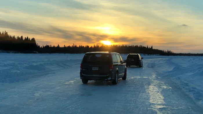 Deux véhicules s’engagent sur une route de glace au coucher du soleil.
