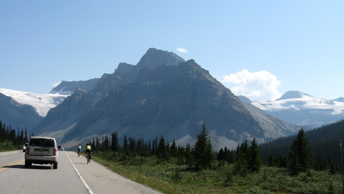 Des voitures et des cyclistes sur une route au milieu des montagnes