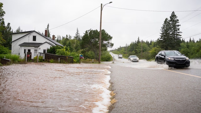 Deux voitures circulent lentement sur la route recouverte d'eau.