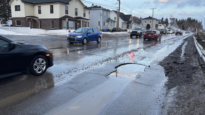 Un nid-de-poule sur une rue au printemps avec des autos.