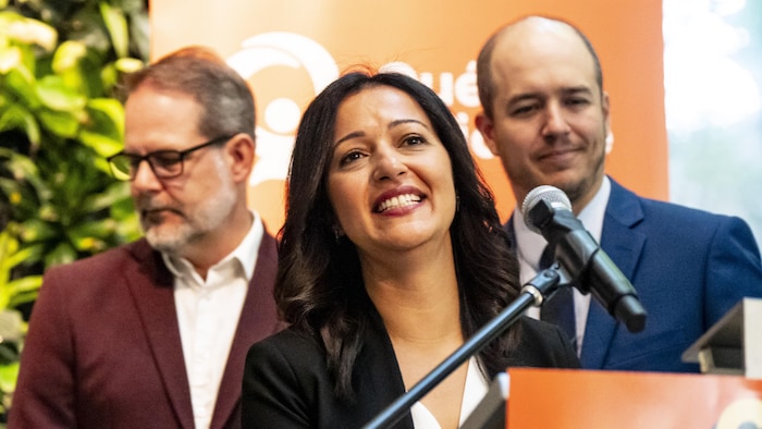 Les trois personnes se tiennent derrière un micro, Ruba Ghazal au milieu.