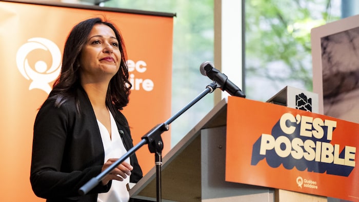 Ruba Ghazal derrière un lutrin orné du slogan de Québec solidaire, « C'est possible ».