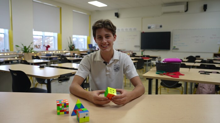 Une personne assise à une table tient un cube Rubik.
