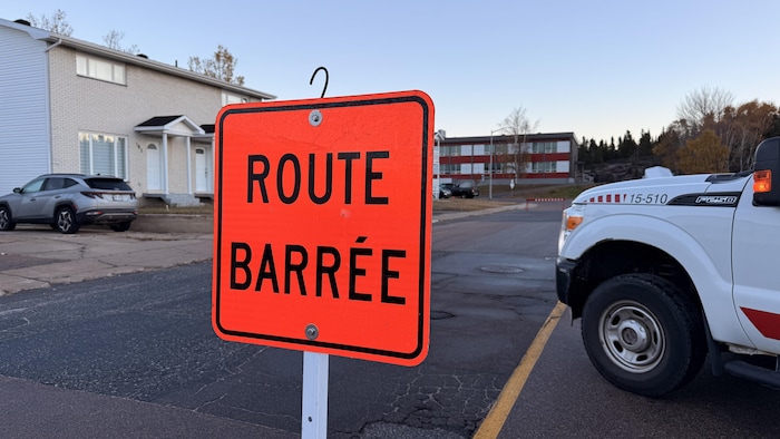 Un panneau routier indique « route barrée » sur une rue qui mène à une école primaire.