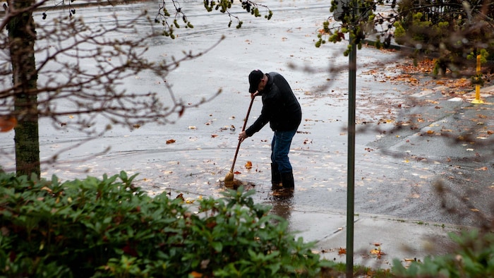 Un homme tente de balayer les feuilles d'une sortie d'une bouche d'égout inondée.