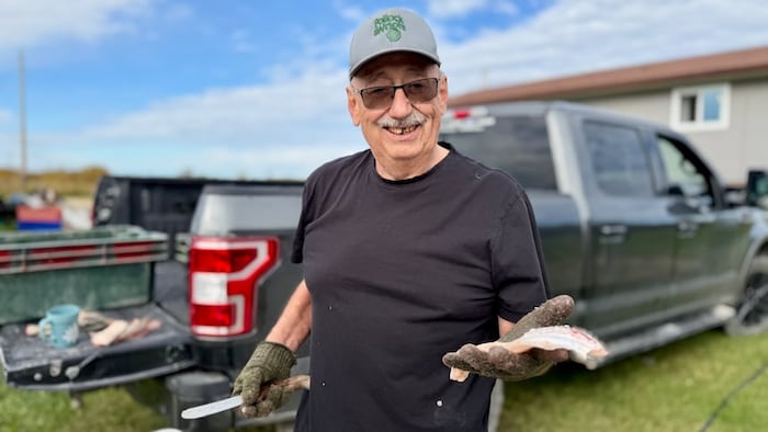 Russell Kirkness tient dans sa main un poisson qu'il a préparé pour le cuisiner.