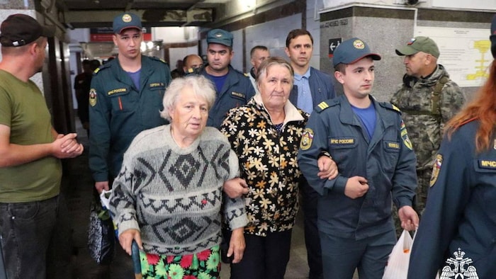 Two elderly men walk with officers at the station. 